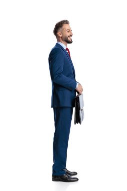 Mavi takım elbiseli neşeli iş adamının elinde evrak çantası ve beyaz arka planda izole edilmiş bir gülümsemeyle ayakta duruşu.