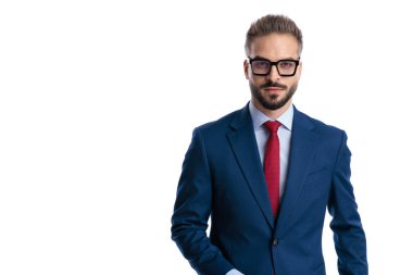 Gözlüklü ve zarif mavi takım elbiseli ciddi genç işadamı beyaz arka planda izole edilmiş bir şekilde ileriye bakıyor.