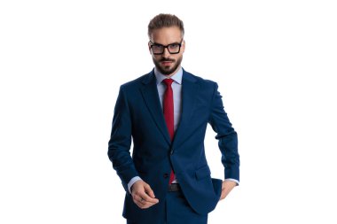 Confident businessman wearing glasses and blue suit walking forward and taking hand out of pocket isolated on white background