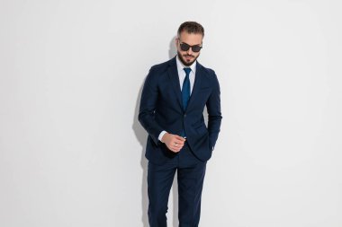 Stylish man in a blue suit and sunglasses standing with hand in pocket on white background