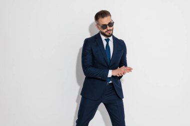 Mysterious man wearing blue suit and sunglasses rubbing palms together while planning on white background
