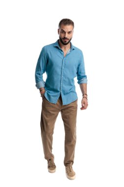 Ciddi sakallı, burun halkalı, kot gömlek giyen ve cebinde ileri doğru adım atan beyaz arka planda yalnız başına ileriye bakan bir adam.