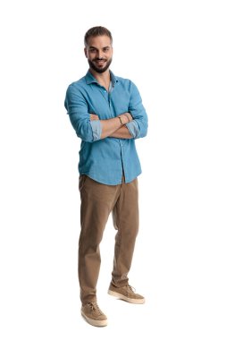 Kolları çapraz duran ve gülümseyen, beyaz arka planda yalnız başına ileriye bakan, kendine güvenen sıradan bir adam.