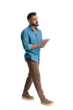 Kot gömlekli şık bir adamın el ele tutuşup yürürken beyaz arka plana baktığı yan görüntü.