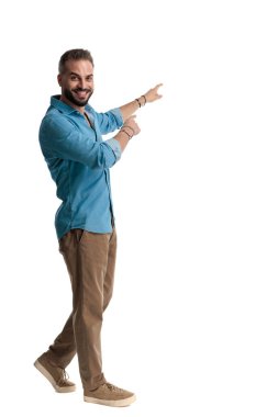 Beyaz arka planda ileri bakan neşeli, sıradan bir adamın yürümesi ve parmaklarını sağa sola göstermesi.