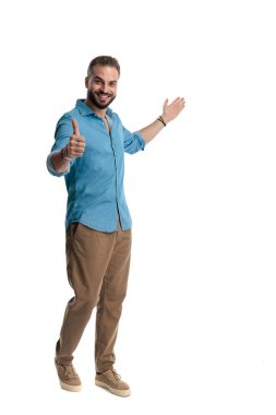 Pozitif, sıradan bir adamın gülümseyip baş parmak hareketi yaptığı ve beyaz arka planda sunum yaptığı tüm vücut pozu.