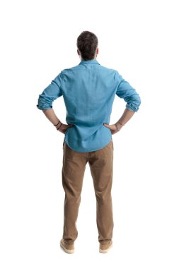 Kot gömlek ve kahverengi pantolon giyen, elleri beyaz arka planda izole kalçalar üzerinde duran kararlı adamın arka planı.