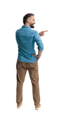 Arka planda gülümseyen sıradan bir adam, beyaz arka planda elleri kalçasında dururken, parmaklarını sağa sola gösteriyor.