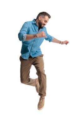 Mutlu sıradan bir adam yüksekten atlıyor ve gülümsüyor ve beyaz arka planda izole bir şekilde havada dans ediyor.