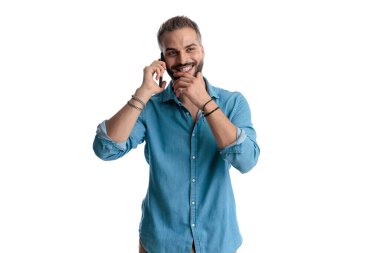 Telefonda konuşurken gülümseyen ve çeneye dokunan neşeli adam beyaz arka planda izole edilmiş.