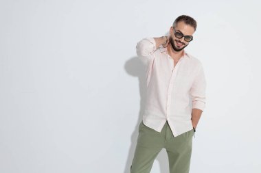 Gözlüklü ve pembe tişörtlü şık sakallı adam, el ele tutuşup el ele gülümserken beyaz arka plana bakıyor.