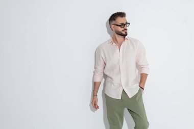 Havalı bir adam cepte duruyor ve beyaz arka plana karşı yan gözle bakıyor.