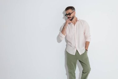 Dalgın bir adam beyaz arka plana bakarken dudağa dokunuyor ve düşünüyor.