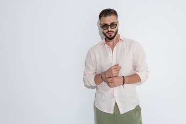 Takı ve güneş gözlüğü takan modacı beyaz arka plana bakarken ayakta duruyor.