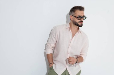 Burun halkalı, güneş gözlüklü havalı bir adam beyaz arka planda el ele poz verirken gözlerini kaçırıyor.