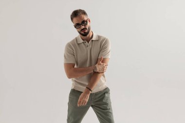 Gri arka plana bakarken polo tişört ve gözlük takan kendine güvenen bir adam.