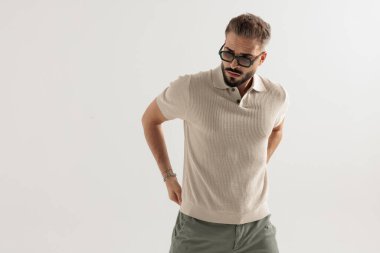 Gözlüklü ve bej tişörtlü moda bir adam pantolonu ayarlıyor ve beyaz arka planda izole edilmiş bir yer arıyor.