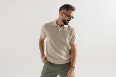 Güneş gözlüğü ve bej renkli polo tişört takan şık bir adam gri arka planda el ele geziyor.