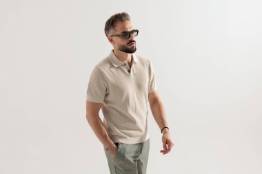 Bej renkli polo gömlek ve güneş gözlüğü takan şık bir adam el ele yürüyor ve beyaz arka planda yer almak istiyor.
