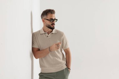 Güneş gözlüğü takıp beyaz arka planda el ele poz veren şık bir adam.