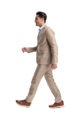 Bej renkli keten takım elbiseli mutlu bir adamın beyaz bir arkaplanda yürüdüğünü ve gülümsediğini görmek.