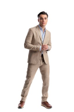 Bej renkli keten takım elbise giyen kendine güvenen bir adam beyaz bir arka plana bakarken ellerini birbirine sürtüyor.