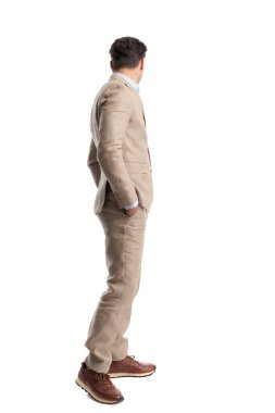 Elleri ceplerinde duran ve beyaz arka planda tek başına duran şık bir adamın yan görünüşü.