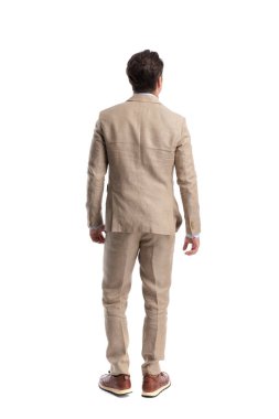 Beyaz arka planda sakince duran bej takım elbiseli şık bir adam.