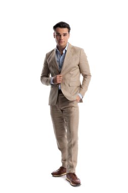 Bej renkli keten takım elbiseli zeki bir adam beyaz arka planda ilerlerken ceketini diker ve ayarlar.