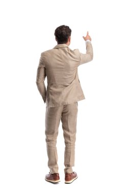 Beyaz arka planda, bej takım elbiseli akıllı bir adamın parmağı yukarı bakıyor.