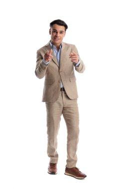 Bej renkli keten takım elbiseli mutlu adam beyaz arkaplan arkaplanına bakarken iki parmağını öne uzatıp işaret ediyor.