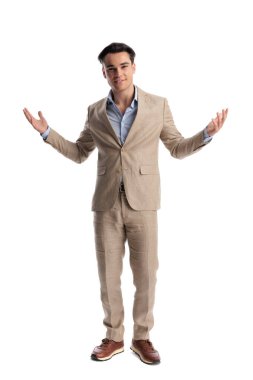 Bej renkli keten takım elbiseli hoş geldin adamı kolları açık, gülümsüyor ve beyaz arka planda ileriye bakıyor.
