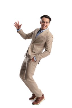 Tutkulu bir adam bej renkli keten bir takım elbise giyiyor. Arkaya yaslanıp elini cebine atıyor ve beyaz bir arkaplanda ileriye bakıyor.