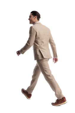 Beyaz arka planda yürüyen bej keten takım elbiseli gülümseyen adamın yan görüntüsü