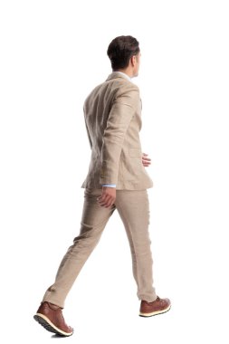 Beyaz arka planda yürüyüp giden bej keten takım elbiseli, akıllı, sıradan bir adamın arkadan görünüşü.