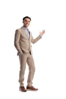 Dost canlısı, bej renkli keten takım elbiseli, cebinde duran ve beyaz arka planda ileriye doğru bakan bir adam.