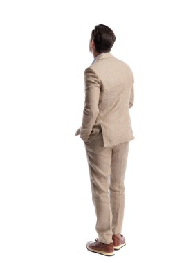 Arkaya bakan zarif bir adam keten bir takım elbise giyiyor, el ele duruyor ve beyaz arka planda izole bir şekilde yüzünü çeviriyor.