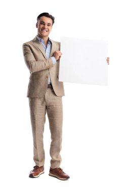 Şık keten takım elbiseli neşeli bir adam iki eliyle büyük beyaz bir tahta tutuyor, gülümsüyor ve beyaz arka planda tek başına ileriye bakıyor.