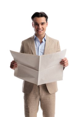 Bej renkli keten takım elbiseli neşeli bir adam elinde boş bir gazeteyle beyaz arka plana bakıyor.