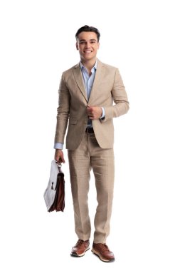 Kahverengi deri evrak çantası taşıyan bej takım elbiseli başarılı bir adam beyaz arka planda tek başına ileriye bakıyor.