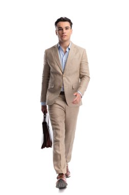 Moda adamı, elinde deri bir çantayla yürür ve öne doğru yürür ve beyaz arka planda izole bir şekilde ileriye bakar.