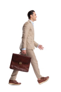Deri evrak çantasıyla yürüyen ve öne çıkan mutlu bir adamın beyaz arka planda izole bir şekilde ileriye baktığı yan bakış.