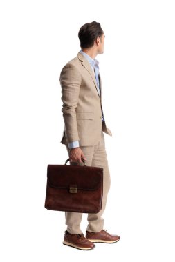 Kahverengi deri evrak çantası tutan ve beyaz arka planda izole edilmiş, bej keten takım giyen zarif bir adamın arka görüntüsü.