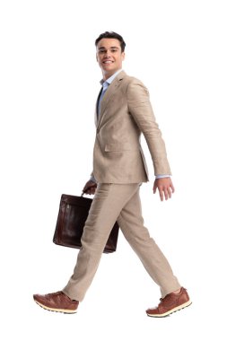 Deri evrak çantasıyla yürüyen ve adım atan gülümseyen bir adamın beyaz arka planda izole bir şekilde ileriye bakması.