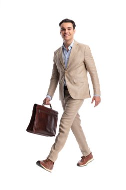 Beyaz arka planda kahverengi deri evrak çantası olan bej renkli takım elbiseli neşeli bir adam yürüyordu ve ileriye bakıyordu.