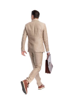Bej renkli keten takım elbiseli modern bir adamın beyaz arka planda izole edilmiş deri çantasıyla yürüyüp gidişinin arka planı.