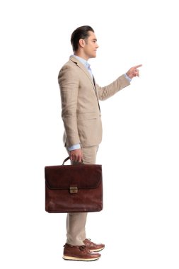 Beyaz arka planda kahverengi deri evrak çantası tutan bej renkli keten takım elbiseli zeki bir adamın yan görüntüsü.