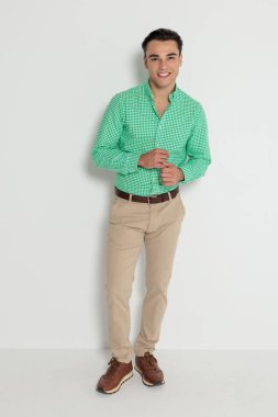 Kareli gömlek giyen yakışıklı bir adam beyaz arka plana bakarken kollarını ayarlıyor ve hazırlanıyor.