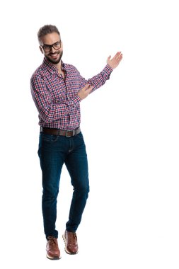 Neşeli, gözlüklü ve ekose gömlekli bir adam iki eliyle sunarken gülümsüyor ve beyaz arka planda tek başına ileriye bakıyor.