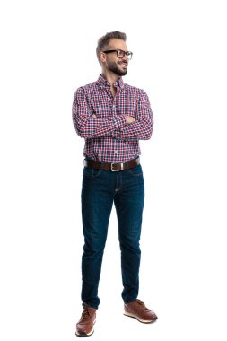 Gözlüklü ve ekose gömlekli neşeli adam beyaz arka planda izole edilmiş bir tarafa bakarken tüm vücudu çapraz kollarla ayakta duruyor.